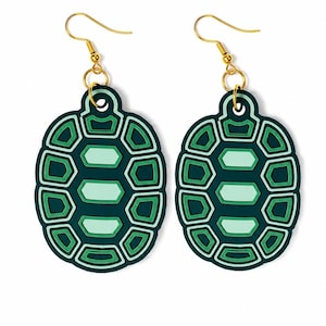 Puede incluir: Un par de pendientes colgantes con un diseño de caparazón de tortuga. Cada pendiente tiene forma de caparazón ovalado con un patrón geométrico en verde oscuro, verde medio y verde claro. Los pendientes cuelgan de ganchos de metal dorado.