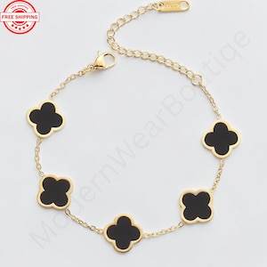 May include: A gold-tone chain bracelet featuring five evenly spaced black clover-shaped charms with gold-tone borders. The bracelet includes a lobster claw clasp, an adjustable extender chain, and a small rectangular tag stamped with 18KGP.