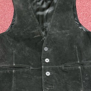May include: A black suede vest with a V-neck and three button closure. The vest has two front pockets and a satin lining. The label reads "BEYOND".