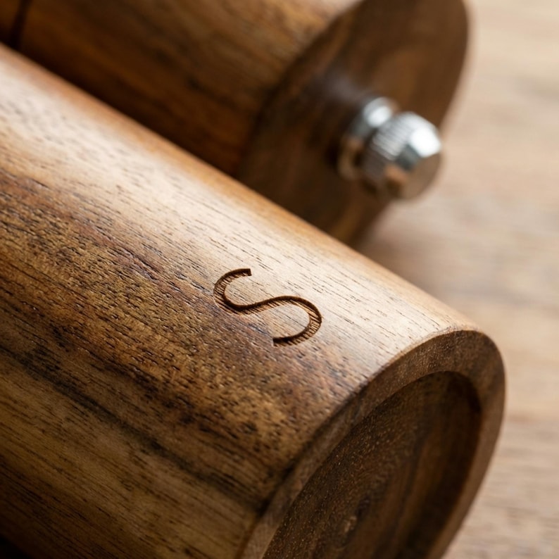 Close up of acacia wood salt grinder engraved S letter detail, warm natural wood grain texture, premium kitchen accessory