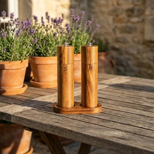 Acacia wood salt and pepper mills flat lay with fresh tomatoes, rosemary, whole peppercorns and olive oil on rustic wooden surface