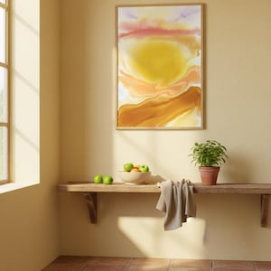 Può includere: Una stampa artistica astratta incorniciata, con una tavolozza di colori gialli e arancioni, è appesa sopra una mensola di legno. La mensola espone una ciotola di frutta, una pianta in vaso e un asciugamano beige piegato. Ci sono anche mele verdi.