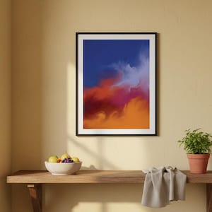 Può includere: Stampa artistica astratta in una cornice nera. L'opera presenta una miscela di colori, tra cui blu, arancione, rosso e viola, creando una composizione dinamica e vibrante. La stampa è esposta su una mensola di legno marrone chiaro.