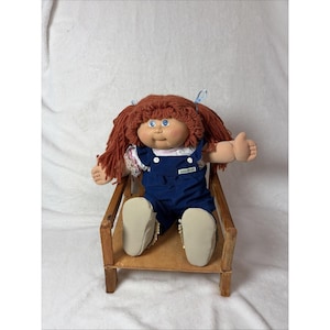 May include: A rustic wooden sign with the text "Welcome" in a handwritten style. The sign is painted white with a distressed finish, and features a decorative floral element in the corner. The background is a blurred image of a wooden surface.