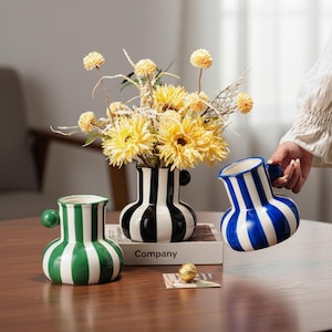 Puede incluir: Un juego de tres tazas de cerámica con un acabado mate moteado. Las tazas son de color crema, gris claro y gris oscuro. Cada taza tiene un diseño simple y minimalista y un asa redondeada.