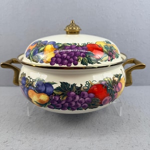 Puede incluir: Olla de esmalte color crema con tapa, adornada con un vibrante diseño de frutas con uvas, manzanas y ciruelas. La olla tiene asas doradas y un pomo a juego en la tapa. Un artículo de menaje de cocina decorativo.