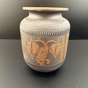 Op de afbeelding: Een donkergrijze keramische vaas met een getextureerd oppervlak en een brede opening. De vaas heeft een ingewikkeld ontwerp van oranjebruine bladeren en wijnranken. De vaas is ongeveer 25 cm hoog.