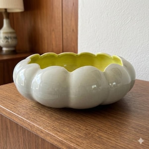 May include: A low, round ceramic bowl with a scalloped, petal-like edge. The exterior of the bowl features a glossy, light gray finish, while the interior is glazed in a vibrant, bright yellow color. The bowl has a smooth, curved silhouette.