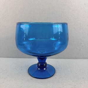 May include: A vibrant blue glass goblet with a rounded bowl and a short stem. The goblet is made of transparent glass, allowing light to pass through. The base is a solid, circular shape. The overall design is simple and elegant.