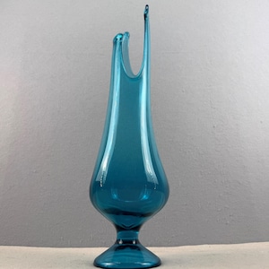 May include: A tall, teal-colored glass vase with a flared top and a slender, elongated body. The vase has a rounded base and a smooth, glossy finish, reflecting light. The overall design is elegant and modern, suitable for decorative purposes.