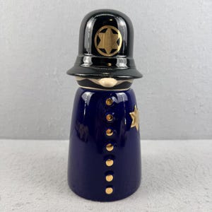Peut inclure: Figurine en céramique représentant un policier. Le corps est bleu marine avec des détails dorés. Le chapeau noir est orné d'une étoile dorée. L'uniforme a des boutons dorés et une étoile dorée, environ 15 cm de haut.