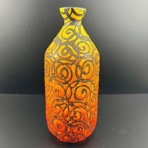May include: A decorative ceramic vase with a unique design. The vase features a gradient of orange and yellow hues, with a black, swirling pattern covering the surface. The vase has a narrow neck and a rounded body, suitable for home decor.