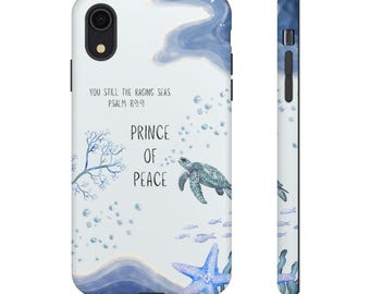 Pode incluir: Uma capa de telefone branca com um design em aquarela com uma tartaruga marinha, uma estrela do mar e o texto "You Still The Raging Seas Salmo 89:9" e "Prince of Peace". A capa tem uma lente de câmera preta.