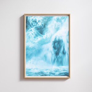 May include: A framed art print featuring a digitally enhanced waterfall scene. The artwork showcases a cascade of water in shades of blue and white, with a blurred, ethereal effect. The print is encased in a light-colored wooden frame.