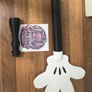 May include: A black 3D-printed handle and a white cartoon hand with three black ovals. A black 3D-printed object and a sticker with the text "Crafted Creations 3D Printing" are also present.