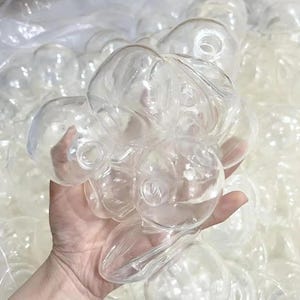May include: A collection of clear, spherical plastic ornaments, each featuring a small circular opening at the top. These hollow, transparent globes are lightweight and designed for crafting or decorative purposes, shown here in a large bulk quantity.