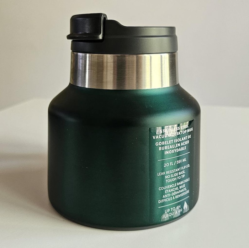 May include: A dark green stainless steel vacuum desktop mug with a black flip lid and a silver rim. A label on the front displays the text: STAINLESS STEEL VACUUM DESKTOP MUG, 20 FL / 591 ML, LEAK RESISTANT FLIP LID, NO SLIDE BASE, TOUGH TO TIP, UP TO 4H.
