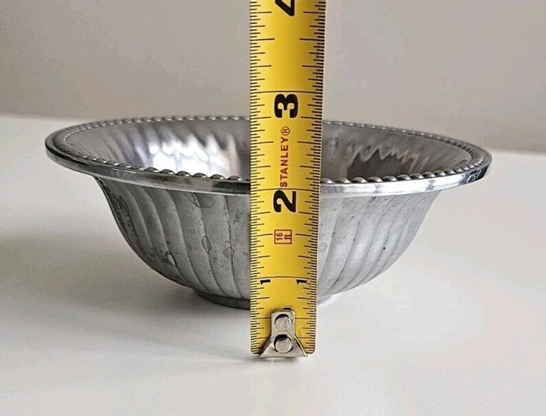 Puede incluir: Un peque&ntilde;o cuenco plateado con un borde con cuentas y un exterior acanalado. El cuenco mide aproximadamente 7,6 cm de alto, medido con una cinta m&eacute;trica amarilla. El cuenco tiene un dise&ntilde;o simple y elegante.