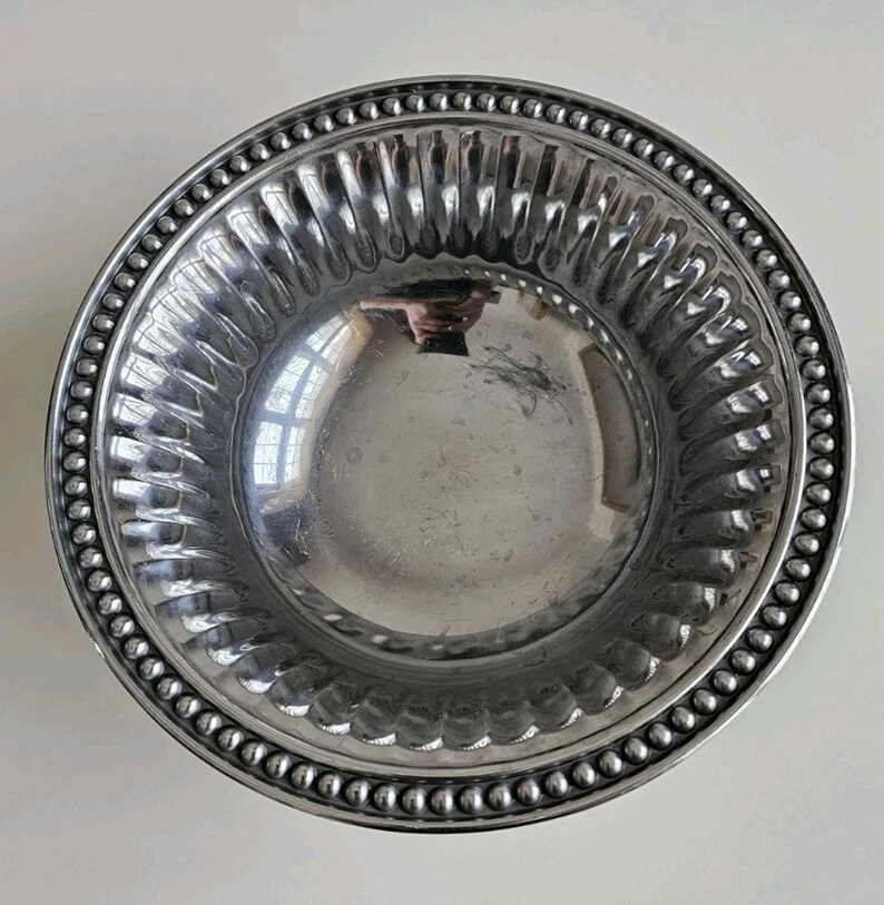 Puede incluir: Un cuenco plateado con un borde de cuentas y un dise&ntilde;o interior acanalado. El cuenco tiene una superficie reflectante, y el borde est&aacute; decorado con peque&ntilde;as cuentas espaciadas uniformemente. El dise&ntilde;o acanalado a&ntilde;ade textura al interior del cuenco.