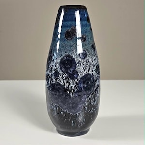 May include: A tall, tapered ceramic vase featuring a crystalline glaze with a gradient transition from deep black at the base to a vibrant blue at the top. The surface is decorated with distinct, star-like crystalline patterns in dark blue.