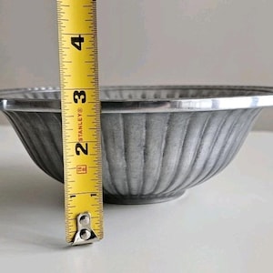 Puede incluir: Un cuenco de metal gris con un dise&ntilde;o acanalado y un borde plateado. El cuenco mide aproximadamente 7,6 cm de alto, medido con una cinta m&eacute;trica amarilla. El cuenco est&aacute; sobre una superficie blanca.