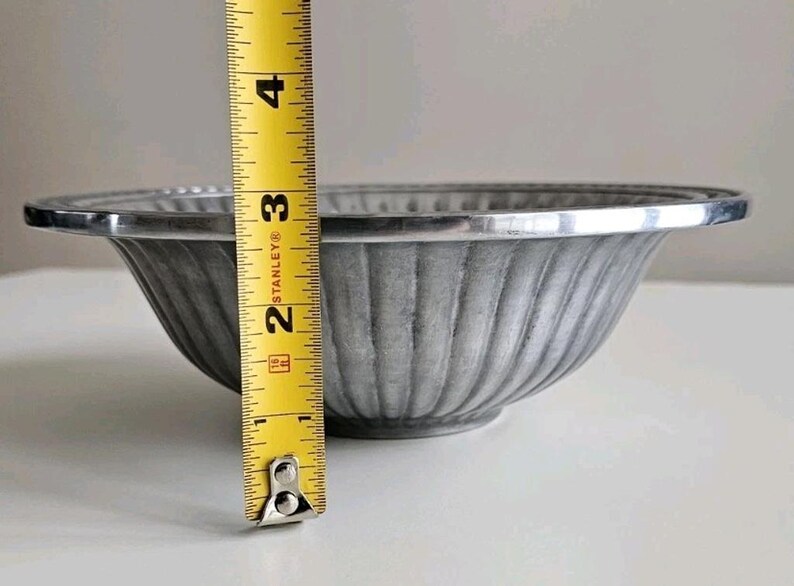 Puede incluir: Un cuenco de metal gris con un dise&ntilde;o acanalado y un borde plateado. El cuenco mide aproximadamente 7,6 cm de alto, medido con una cinta m&eacute;trica amarilla. El cuenco est&aacute; sobre una superficie blanca.