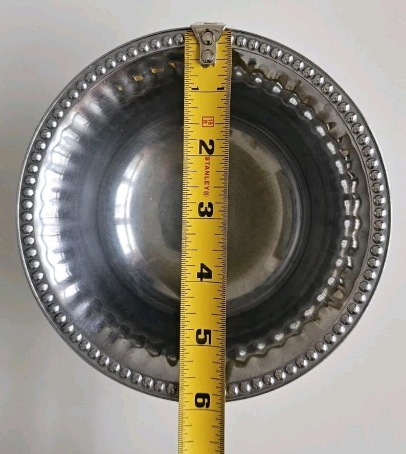 Puede incluir: Un cuenco de metal plateado brillante con un borde con cuentas. Una cinta m&eacute;trica amarilla Stanley se coloca sobre el cuenco, mostrando un di&aacute;metro de aproximadamente 15 cm.