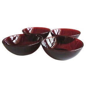 May include: Four dark red glass bowls. Each bowl has a rounded shape with a smooth, glossy finish. The bowls are arranged in a group, showcasing their similar design and color. The bowls are suitable for serving food.