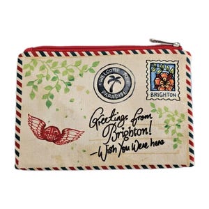 Pu&ograve; includere: Un astuccio rettangolare in tela con cerniera e finiture rosse, progettato per assomigliare a una cartolina vintage. L'astuccio presenta il testo "Greetings from Brighton! - Wish You Were Here" e un francobollo con un motivo floreale.