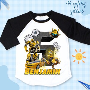 Könnte beinhalten: Weißes und schwarzes Raglan-Shirt mit einem gelb-schwarzen Roboter-Design, einem gelben Auto und dem Namen "BENJAMIN" in Gelb. Das Shirt hat auch den Text "+14 colors sleeve".
