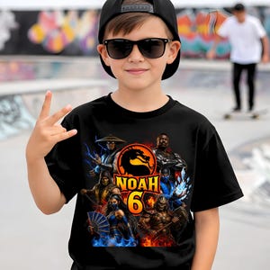 May include: A black short-sleeved t-shirt featuring a colorful graphic print of multiple video game characters surrounding a central dragon logo. The text "NOAH" is printed in yellow above a large orange number "6" in the center of the design.