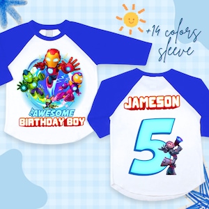 Puede incluir: Una camiseta blanca y azul de estilo ragl&aacute;n con un gr&aacute;fico colorido de personajes de dibujos animados y el texto "THE AWESOME BIRTHDAY BOY". La parte trasera de la camiseta tiene el nombre "JAMESON" y el n&uacute;mero "5".