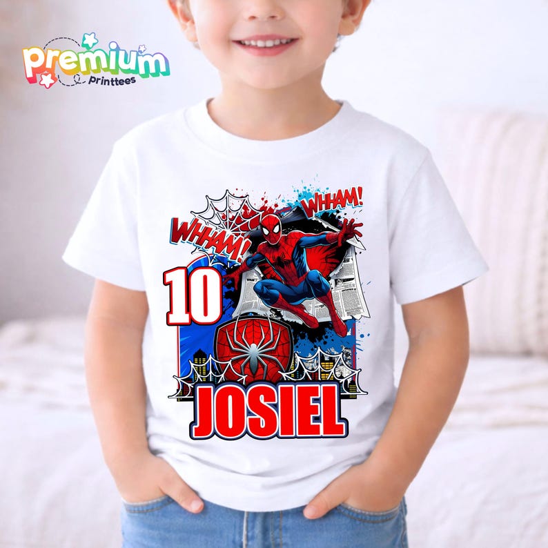 Pu&ograve; includere: T-shirt bianca con grafica colorata di Spider-Man, la scritta "WHAM!" e il numero "10". Il nome "JOSIEL" &egrave; stampato in rosso. La maglietta ha il logo "Premium Printtees".