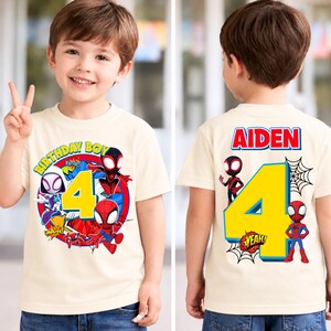 May include: A cream-colored t-shirt featuring a colorful graphic of Spider-Man characters and the number 4. The front of the shirt says "BIRTHDAY BOY" and the back says "AIDEN" with a large yellow number 4.