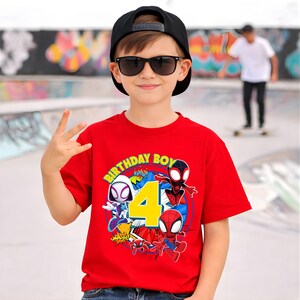 May include: A red t-shirt with a graphic featuring Spider-Man characters and the text "BIRTHDAY BOY 4". The shirt is worn by a person wearing a black cap and sunglasses.
