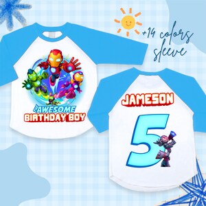 Puede incluir: Camiseta blanca y azul de estilo ragl&aacute;n con un gr&aacute;fico de superh&eacute;roe colorido y el texto "THE AWESOME BIRTHDAY BOY". La parte posterior de la camiseta tiene el nombre "JAMESON" y el n&uacute;mero "5".