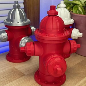 May include: A collection of red, silver, and white miniature fire hydrants. The primary hydrant is a vibrant red, with silver accents on the top and side nozzles. The other hydrants are red and white. The objects are on a wooden surface.