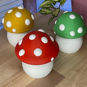 May include: Three mushroom-shaped decorative objects. One is red with white spots, another is yellow with white spots, and the third is green with white spots. All three have white bases and sit on a wooden surface.