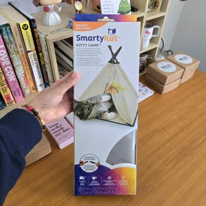 May include: A SmartyKat Kitty Camp cat tent in a box. The box shows a cat inside the tent with a dangling feather toy. The box dimensions are 20.5 x 20.5 x 17.5 inches. The box also has the words "Privacy Solitude".