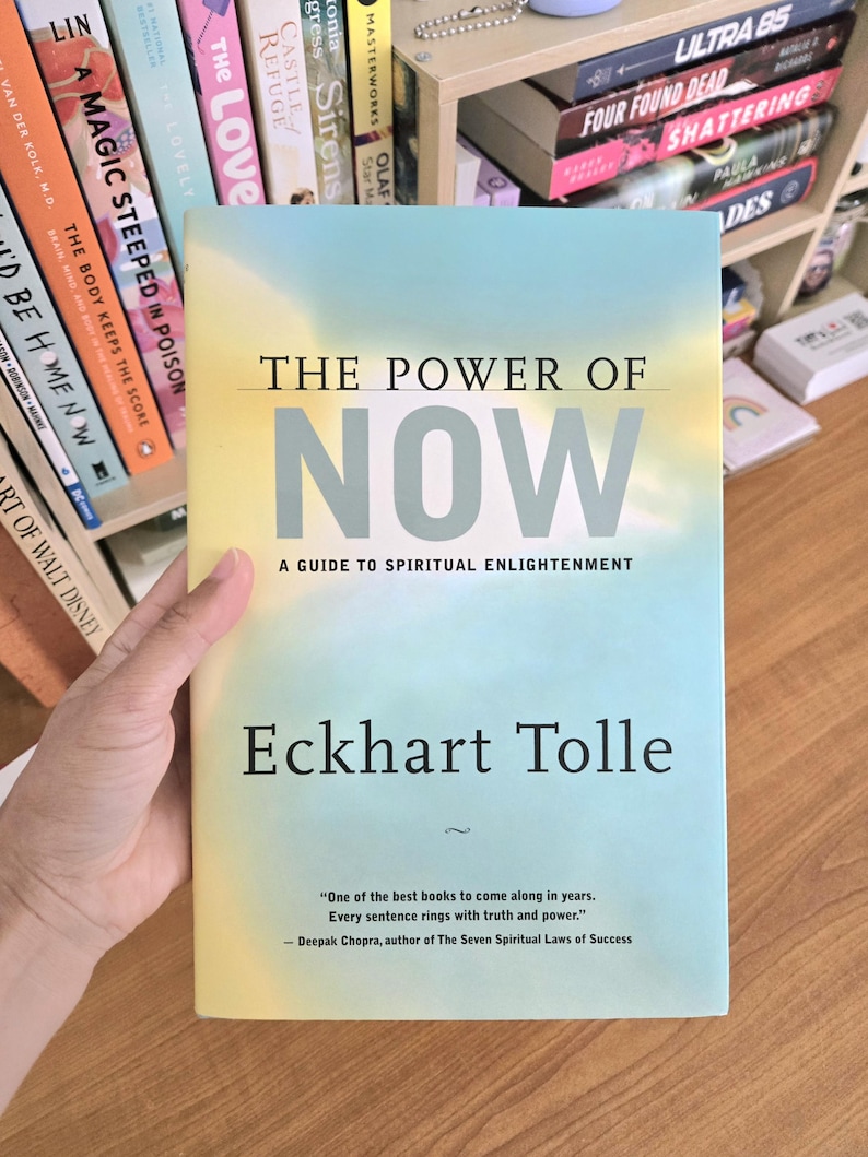 May include: A book titled "The Power of Now" by Eckhart Tolle. The cover has a gradient of yellow and blue with the title in large, bold letters. The subtitle reads "A Guide to Spiritual Enlightenment."
