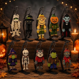 May include: A set of ten hanging Halloween character ornaments, including a mummy, black cat, scarecrow, pumpkin, vampire, witch, skeleton, werewolf, Frankenstein's monster, and zombie, each suspended from a black metal stand.