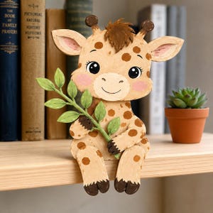 Könnte beinhalten: Eine dekorative Giraffenfigur aus Holz mit hellbraunem Körper, braunen Flecken, rosa Wangen und einer braunen Haartolle. Die Giraffe hält einen grünen Zweig mit Blättern in ihren Vorderhufen und ist so gestaltet, dass sie auf einer Regalplatte sitzt.