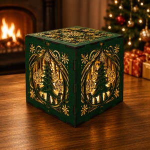 Op de afbeelding: Een donkergroene houten kubuslamp met ingewikkelde lasergesneden ontwerpen van kerstbomen, hangende ornamenten en bloemmotieven. De doos verspreidt een warme interne gloed door de uitsparingen en toont gedetailleerd vakmanschap aan alle zijden.
