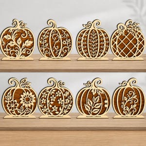 May include: A set of eight wooden pumpkin-shaped decorations, each featuring a unique laser-cut design including floral, leaf, vine, and lattice patterns. Each pumpkin is mounted on a flat rectangular base, showcasing a light wood finish.