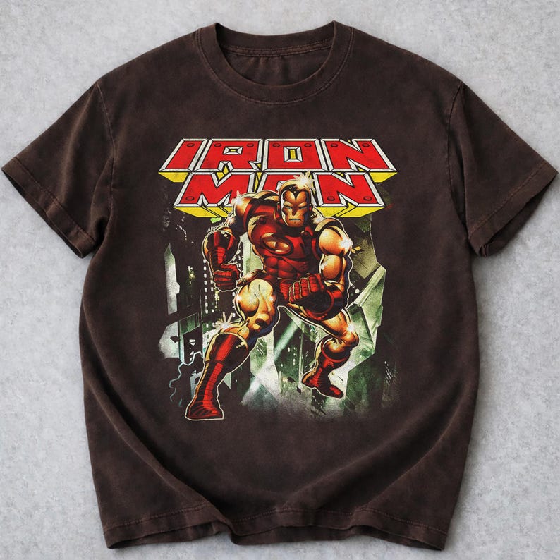 May include: Brown t-shirt with a graphic of Iron Man in a dynamic pose. The design includes the words "IRON MAN" in a bold, red and yellow font. The artwork depicts Iron Man in his classic red and gold armour.