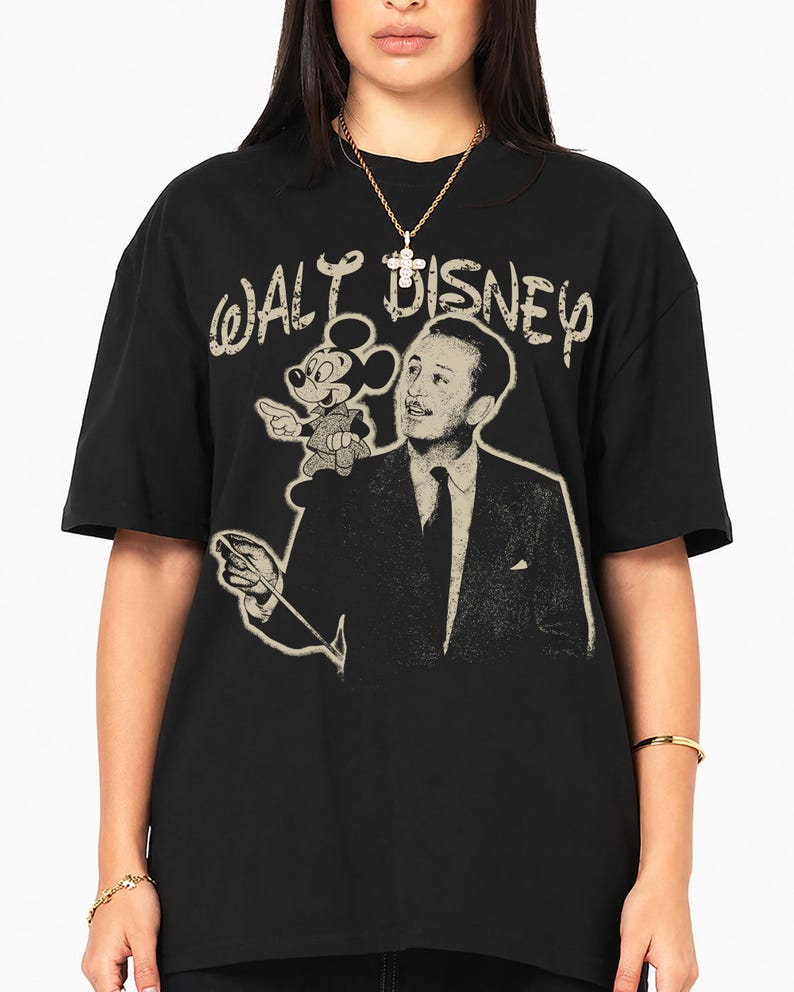 May include: A black short-sleeve t-shirt featuring a graphic print of Walt Disney and Mickey Mouse. The text "WALT DISNEY" is printed in a distressed, light-colored font above the figures. The design includes a portrait of Walt Disney.