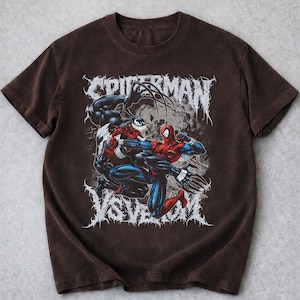 May include: A brown t-shirt with a graphic of Spider-Man fighting Venom. The design includes the words "SPIDERMAN" and "VS VENOM" in a stylized font. The image shows the two characters in a dynamic pose.
