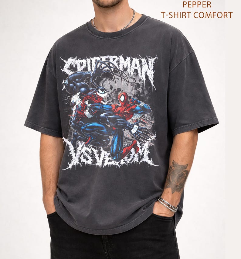 May include: Charcoal grey t-shirt with a graphic of Spider-Man fighting Venom. The design includes the words "SPIDERMAN" and "VS VENOM" in a stylized font. The shirt is labelled "PEPPER T-SHIRT COMFORT" in the upper right corner.