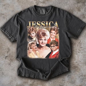 Puede incluir: Camiseta gris oscuro con un diseño de Jessica Fletcher de la serie de televisión "Se ha escrito un crimen". El diseño incluye el nombre "JESSICA" en letras doradas y varias imágenes del personaje. La camiseta es de material suave.