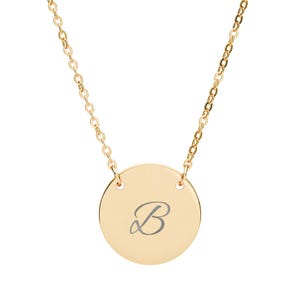 May include: Gold-colored necklace featuring a circular pendant with the letter "B" engraved in a delicate script. The pendant is suspended from a fine chain, creating a simple yet elegant design. The necklace is suitable for everyday wear.